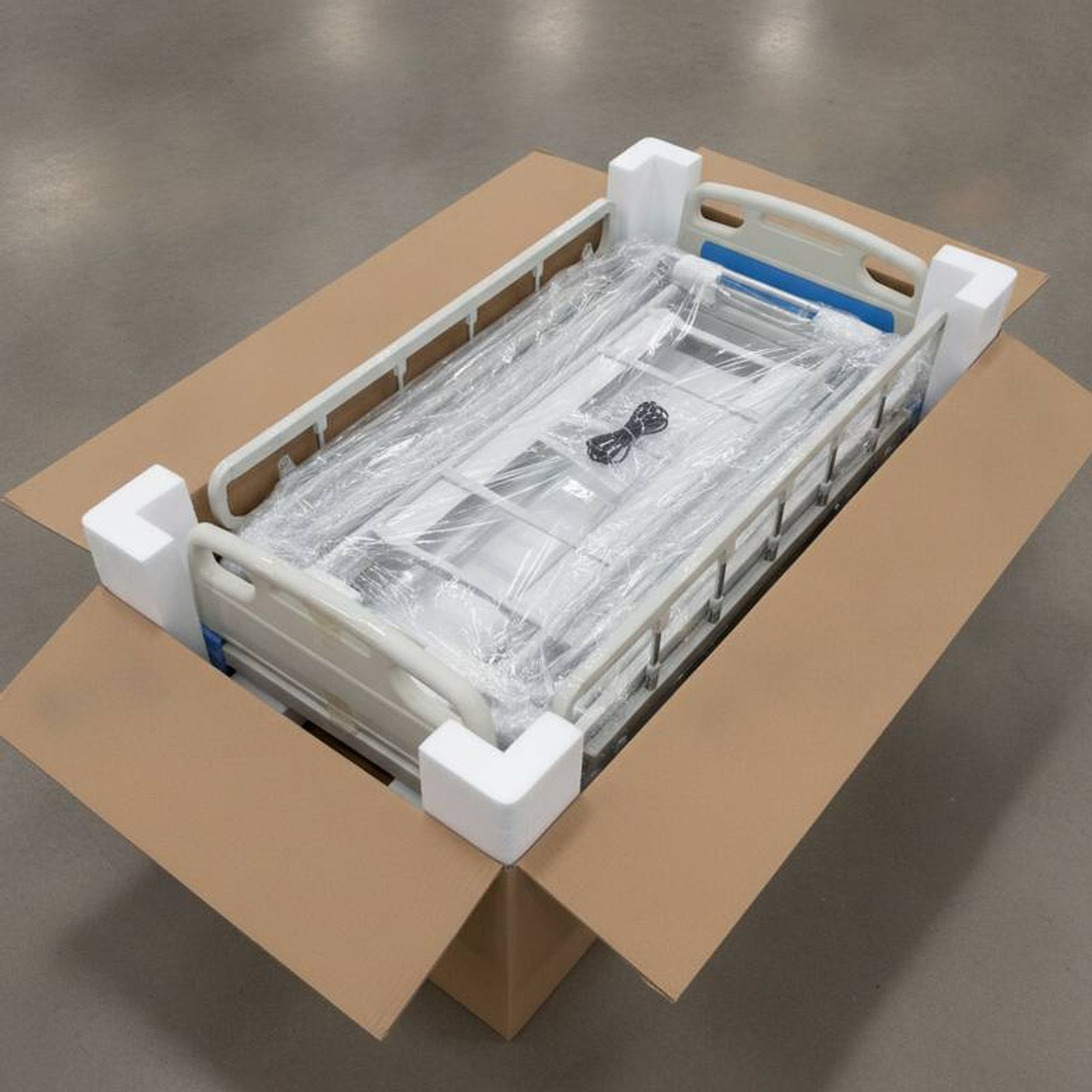 A close-up of a well-packed hospital bed inside an export carton, showing foam corner protectors and secured accessories.