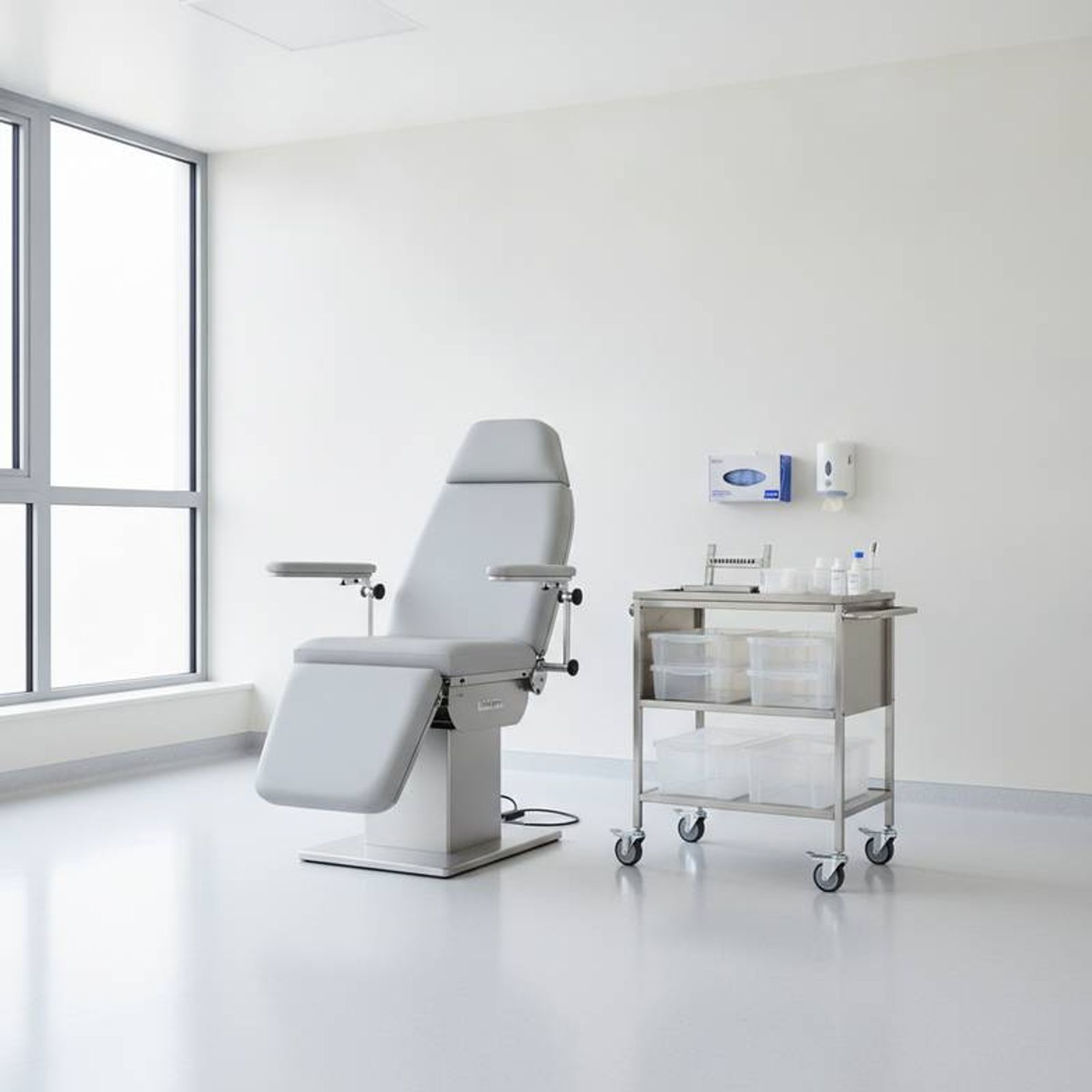 A well-organized clinical zone in a blood collection room, showing a phlebotomy chair, a fully-stocked trolley, and clear space for the phlebotomist to work.