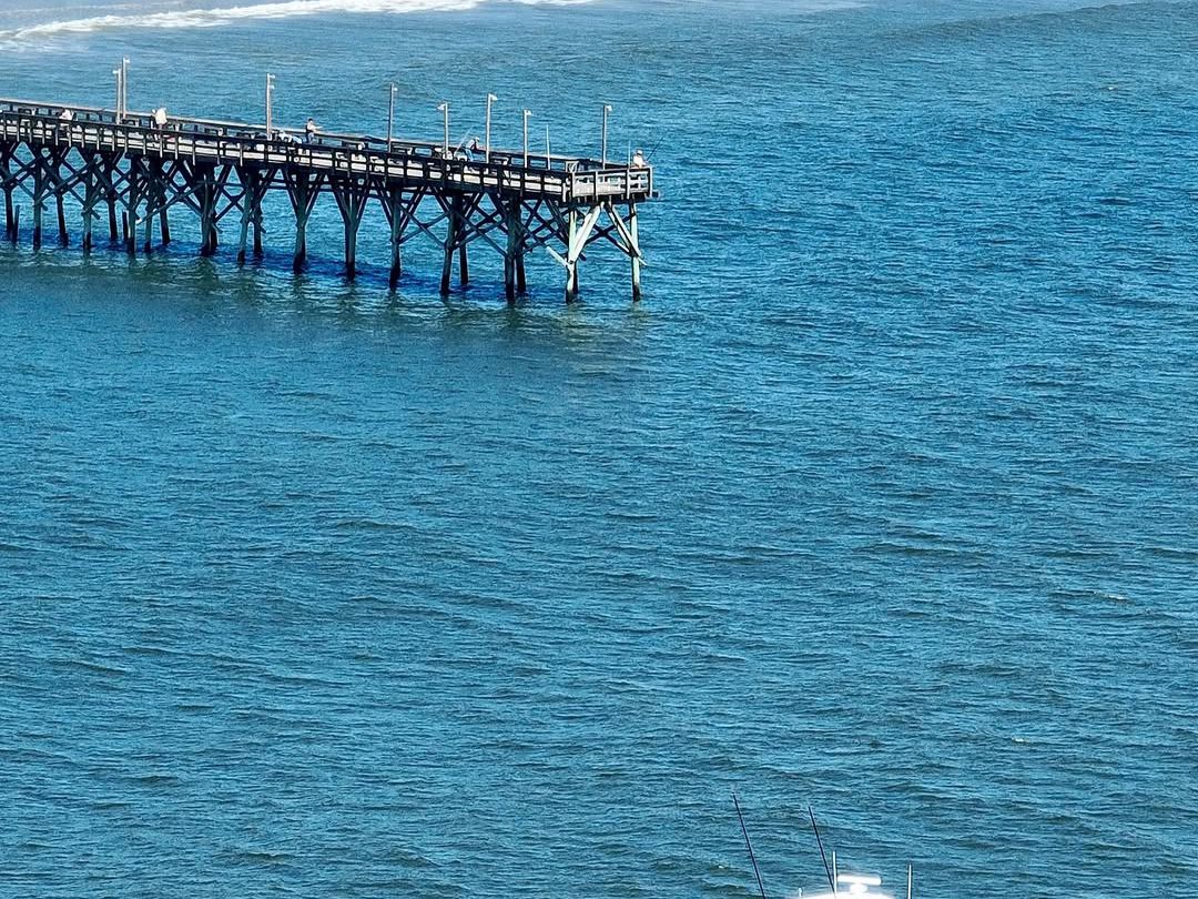 : A fishing boat cruising past Cherry Grove Pier in North Myrtle Beach, offering dolphin cruises and deep-sea fishing adventures.