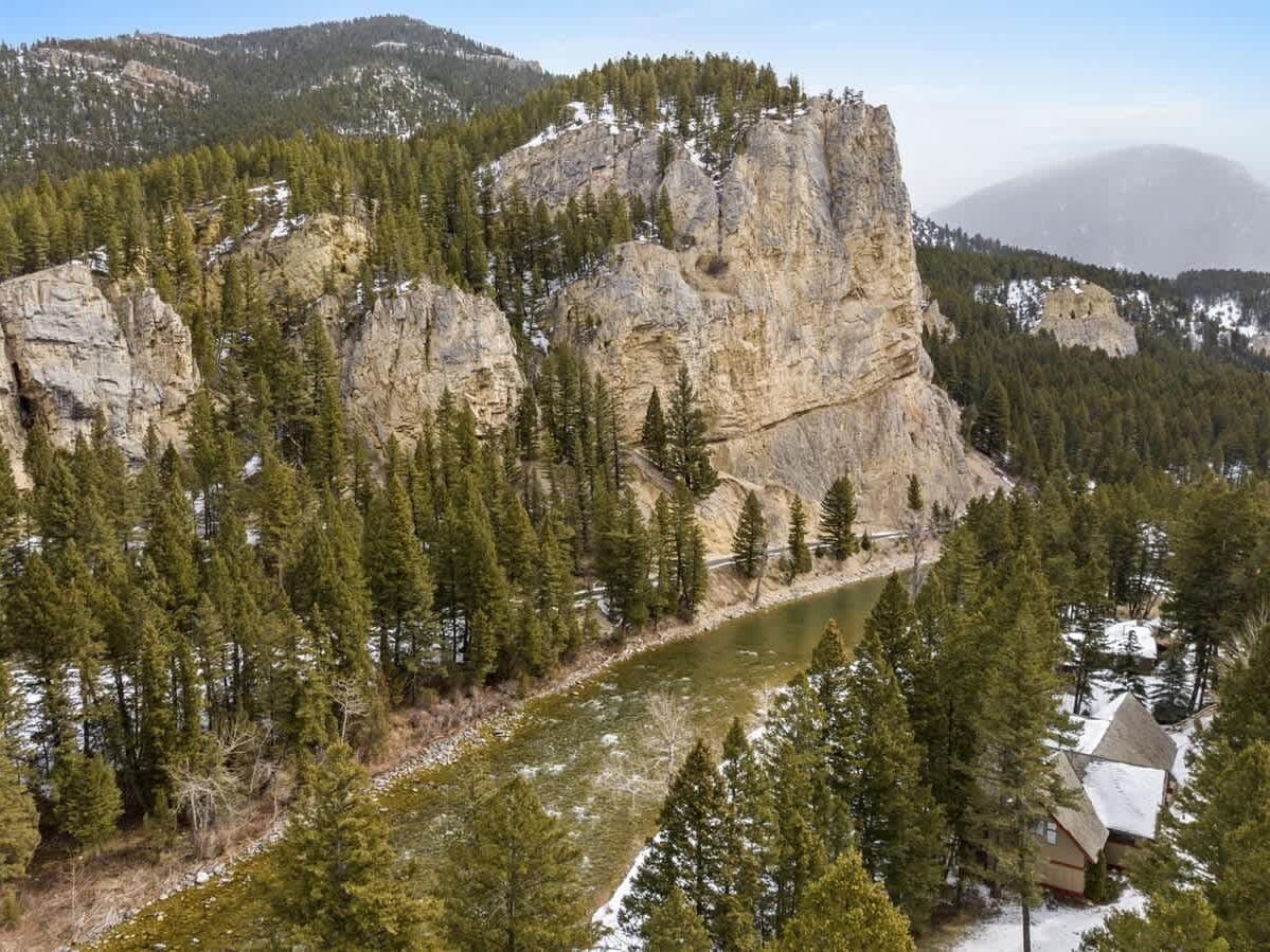 Towering cliffs rise above a winding river surrounded by pine forests in Big Sky, Montana. Light snow dusts the trees, creating a peaceful alpine setting perfect for outdoor adventures.