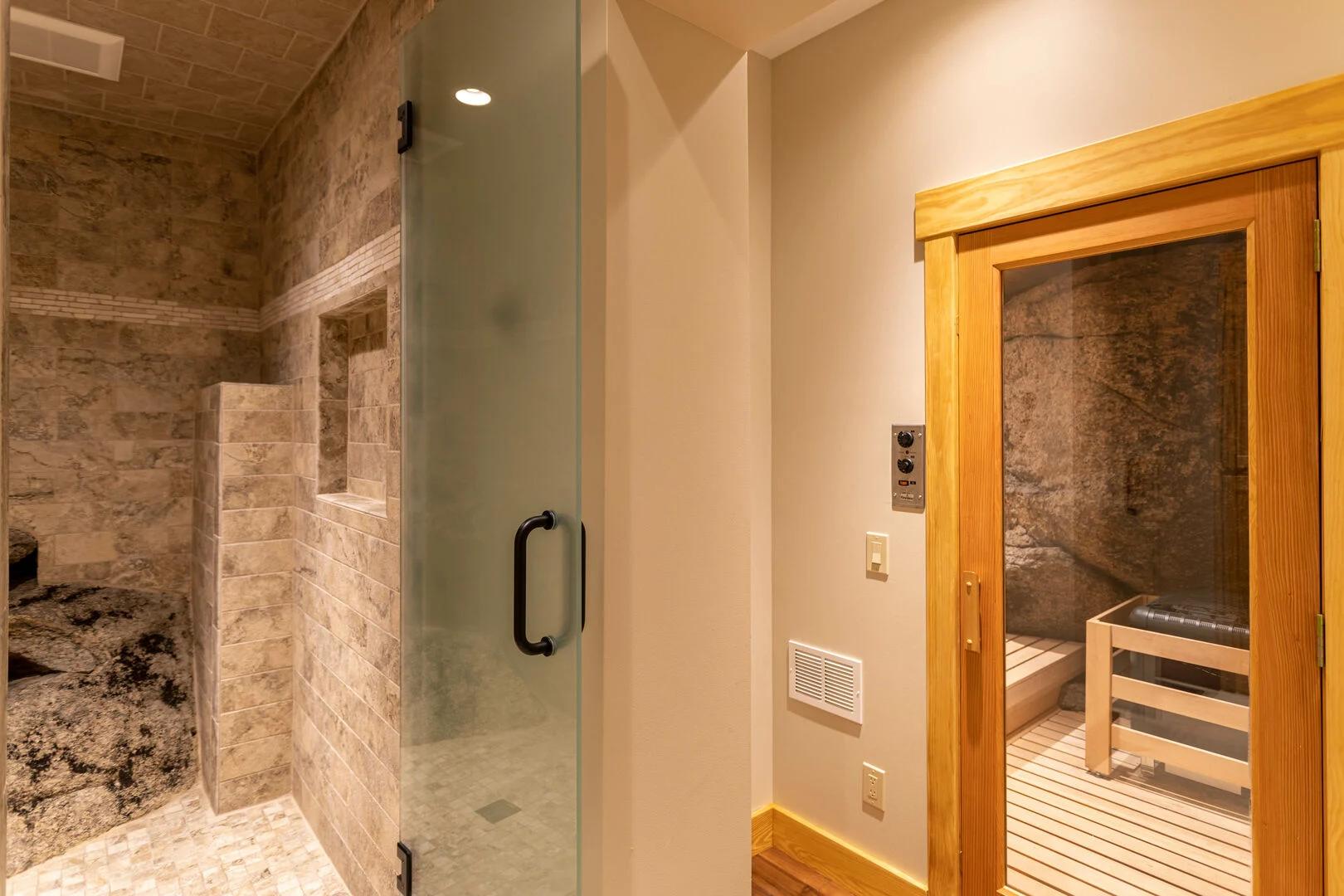 Bathroom of luxury rental with walk-in shower and closed door to sauna with wooden and black bench inside