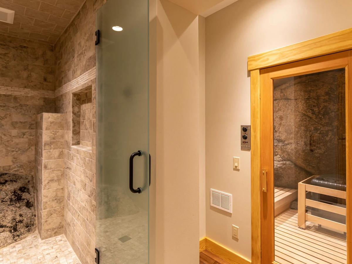 Bathroom of luxury rental with walk-in shower and closed door to sauna with wooden and black bench inside