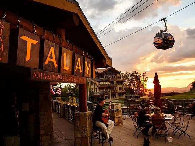 Outdoor patio dining at sunset with live music and gondolas passing overhead. A lively and scenic spot serving Asian-inspired tapas with mountain views.
