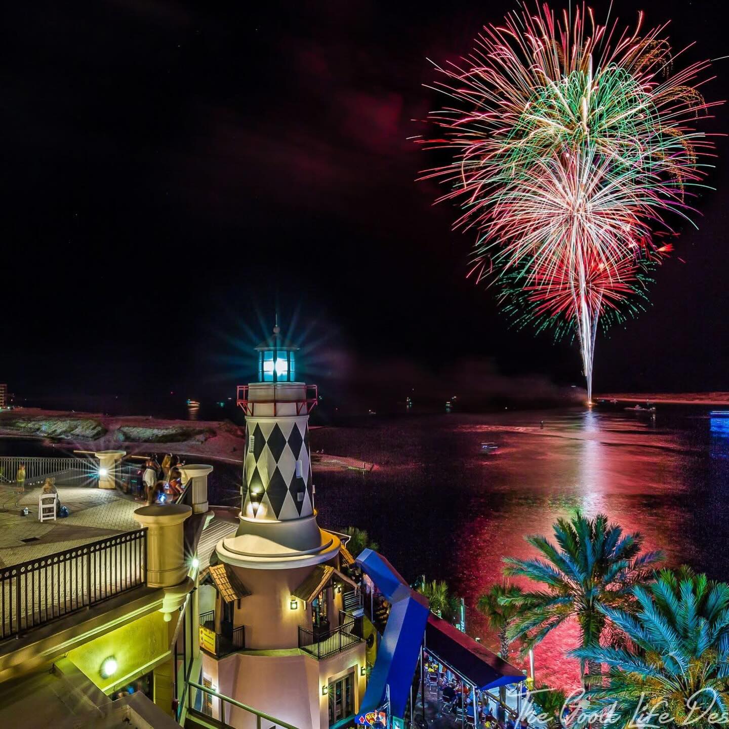 Colorful fireworks light up the night sky over the Destin Harbor, reflecting across the water near the HarborWalk lighthouse. People gather along the waterfront to watch the celebration, creating a lively New Year’s Eve scene by the marina. This image captures the excitement of fireworks over Destin’s harbor at night.