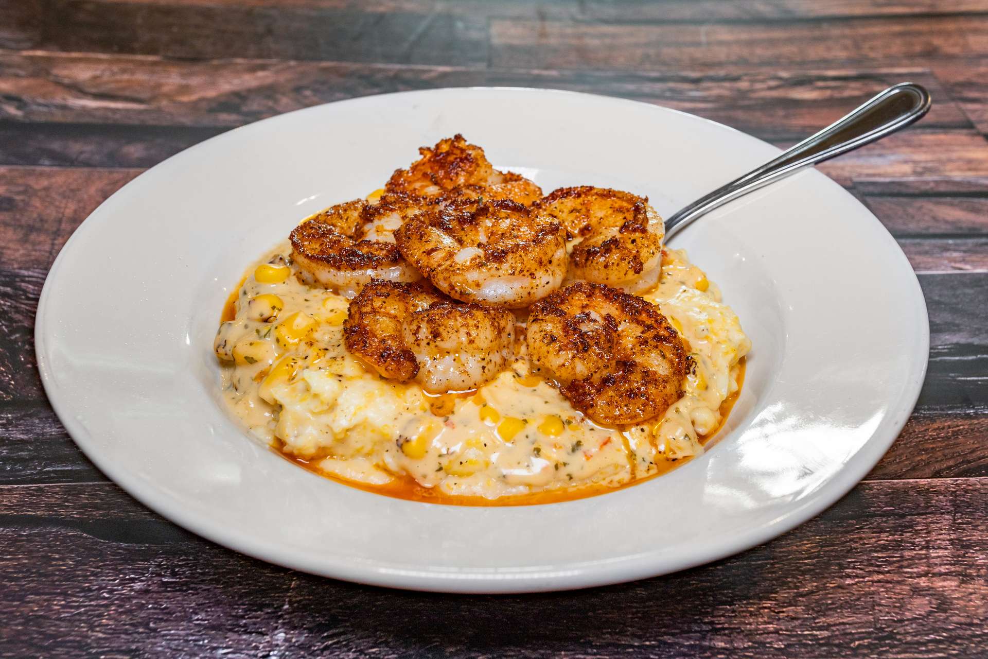 A creamy Southern-style shrimp and grits dish topped with blackened shrimp, served hot and full of flavor. The rustic wooden table and rich seasoning make it a comforting taste of Southern hospitality.