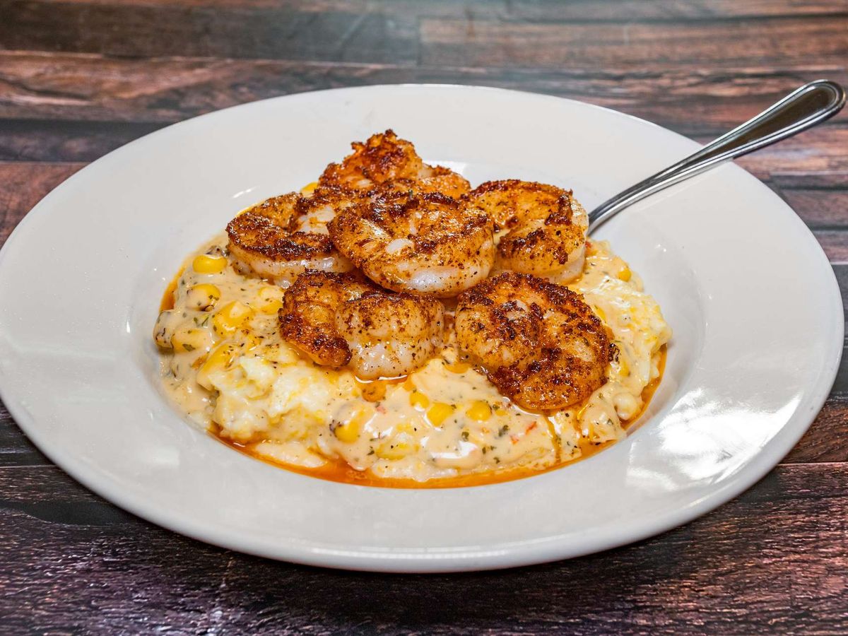 A creamy Southern-style shrimp and grits dish topped with blackened shrimp, served hot and full of flavor. The rustic wooden table and rich seasoning make it a comforting taste of Southern hospitality.