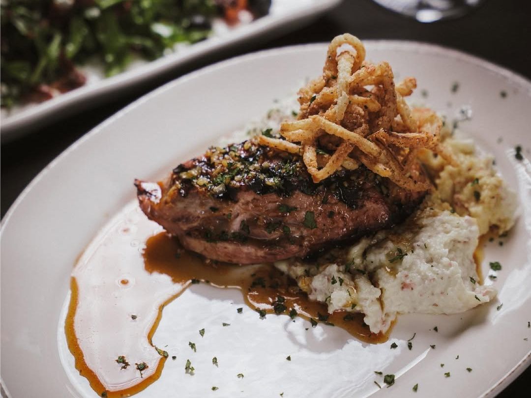 Perfectly grilled pork chop resting on a bed of creamy mashed potatoes with crispy onions on top. This upscale Southern dish is garnished with herbs and served alongside a seasonal salad.
