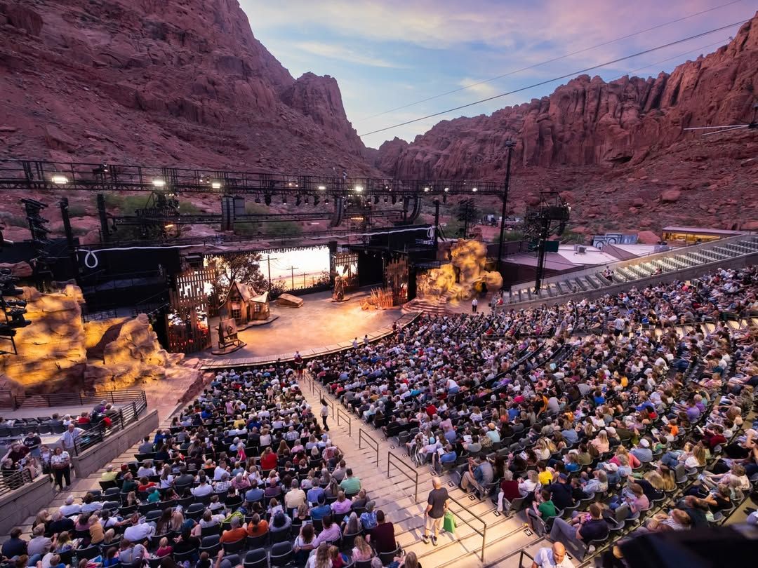 A full crowd enjoys an outdoor performance at Tuacahn Amphitheatre, surrounded by the towering red cliffs of Snow Canyon.