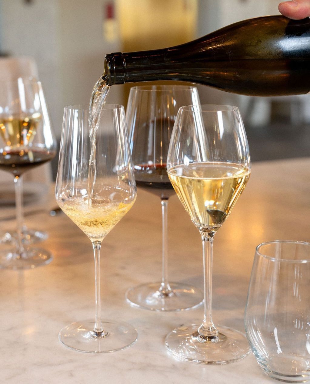 A close-up of white wine being poured into tall tasting glasses at a modern winery table. The soft lighting and clean glassware capture the relaxed feel of a guided wine tasting experience. This image highlights the simple joy of sampling fresh local wines in a calm, inviting setting.