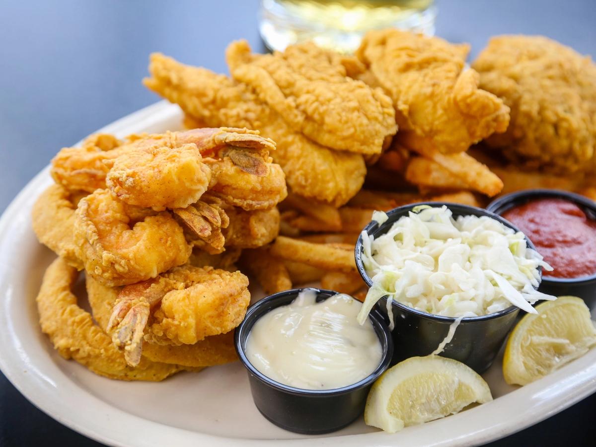A heaping plate of golden fried seafood sits beside dipping sauces, coleslaw, and lemon wedges. Crispy shrimp, fish, and fries make the dish look bold, crunchy, and full of New Orleans flavor. It’s a classic Southern feast that feels fun and filling.