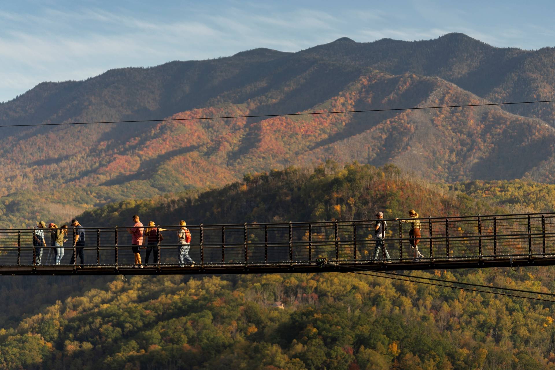 Visitors walk across the famous Gatlinburg SkyBridge suspended high above the Smoky Mountains. The sweeping mountain views and autumn colors create a breathtaking backdrop for photos.