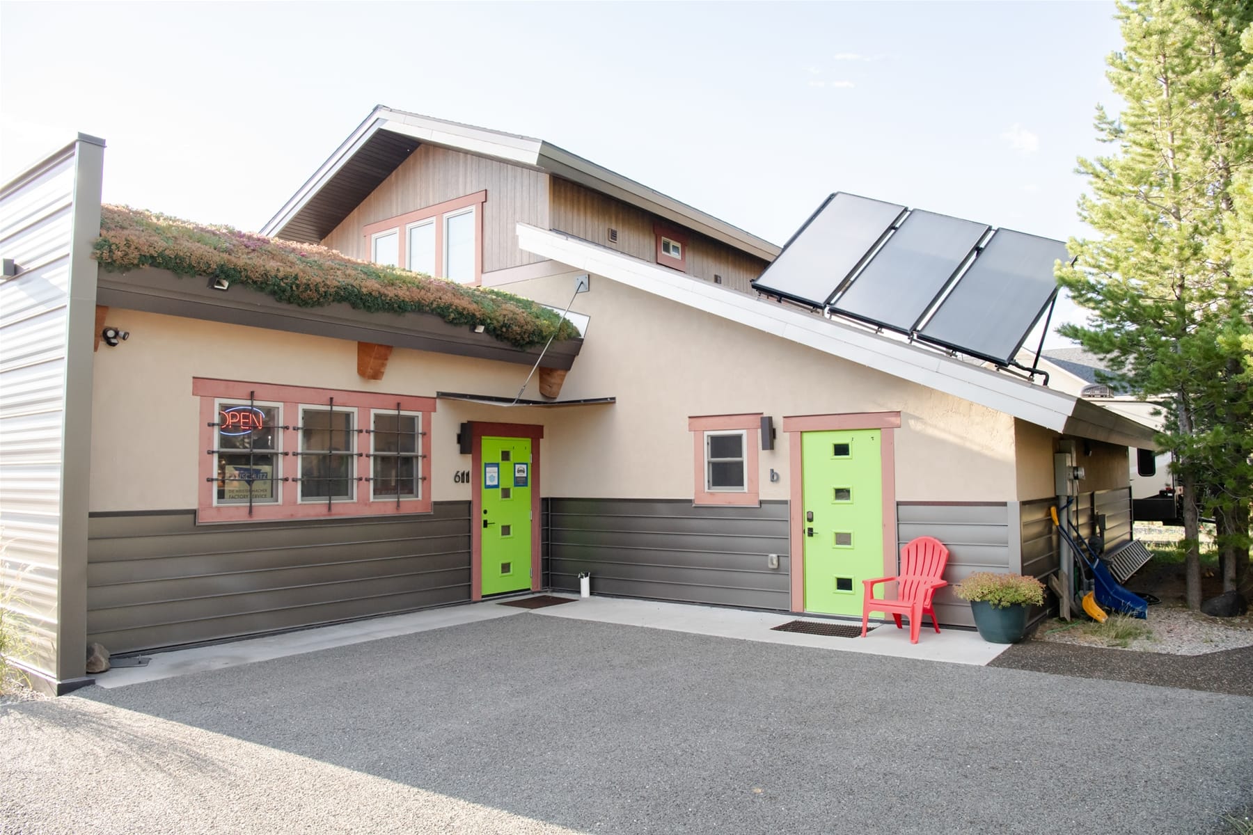 Modern building with bright green doors, solar panels on the roof, and a red chair by the entrance.