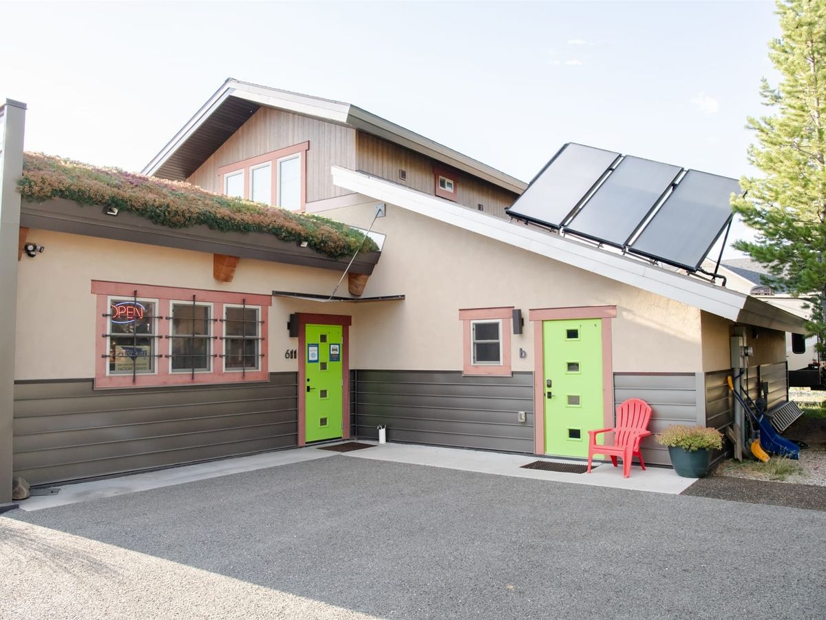 Modern building with bright green doors, solar panels on the roof, and a red chair by the entrance.