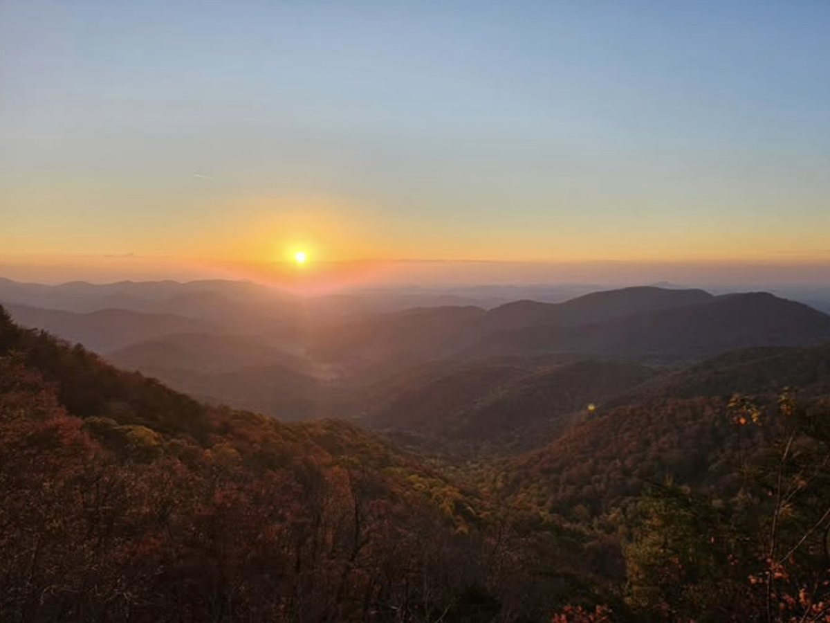 A glowing sunset casts warm light over a vast expanse of rolling mountains and forested valleys in the Appalachian range.