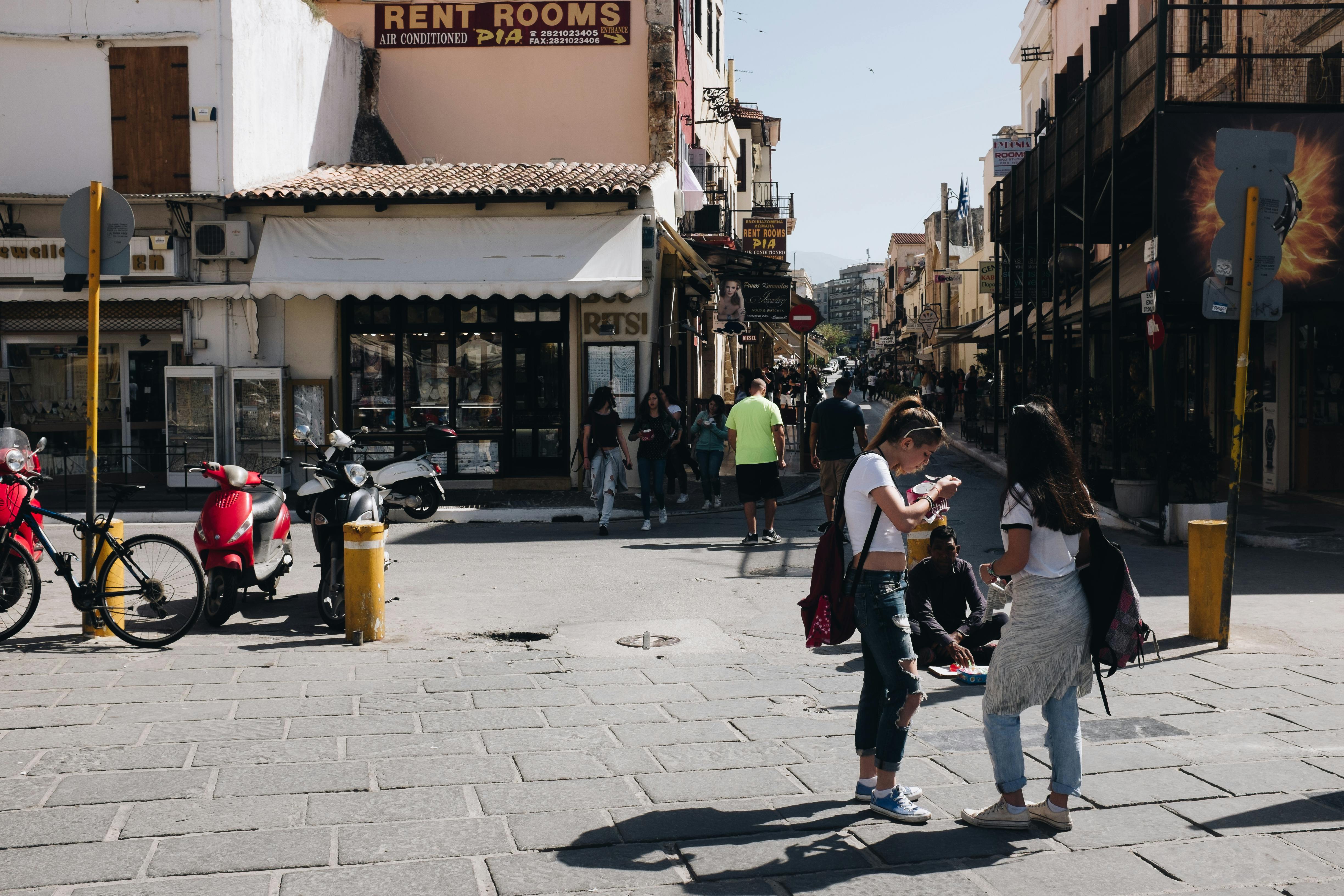A lively city street filled with people walking, chatting, and exploring local shops. Motorbikes line the sidewalk, capturing the energy of everyday travel life.