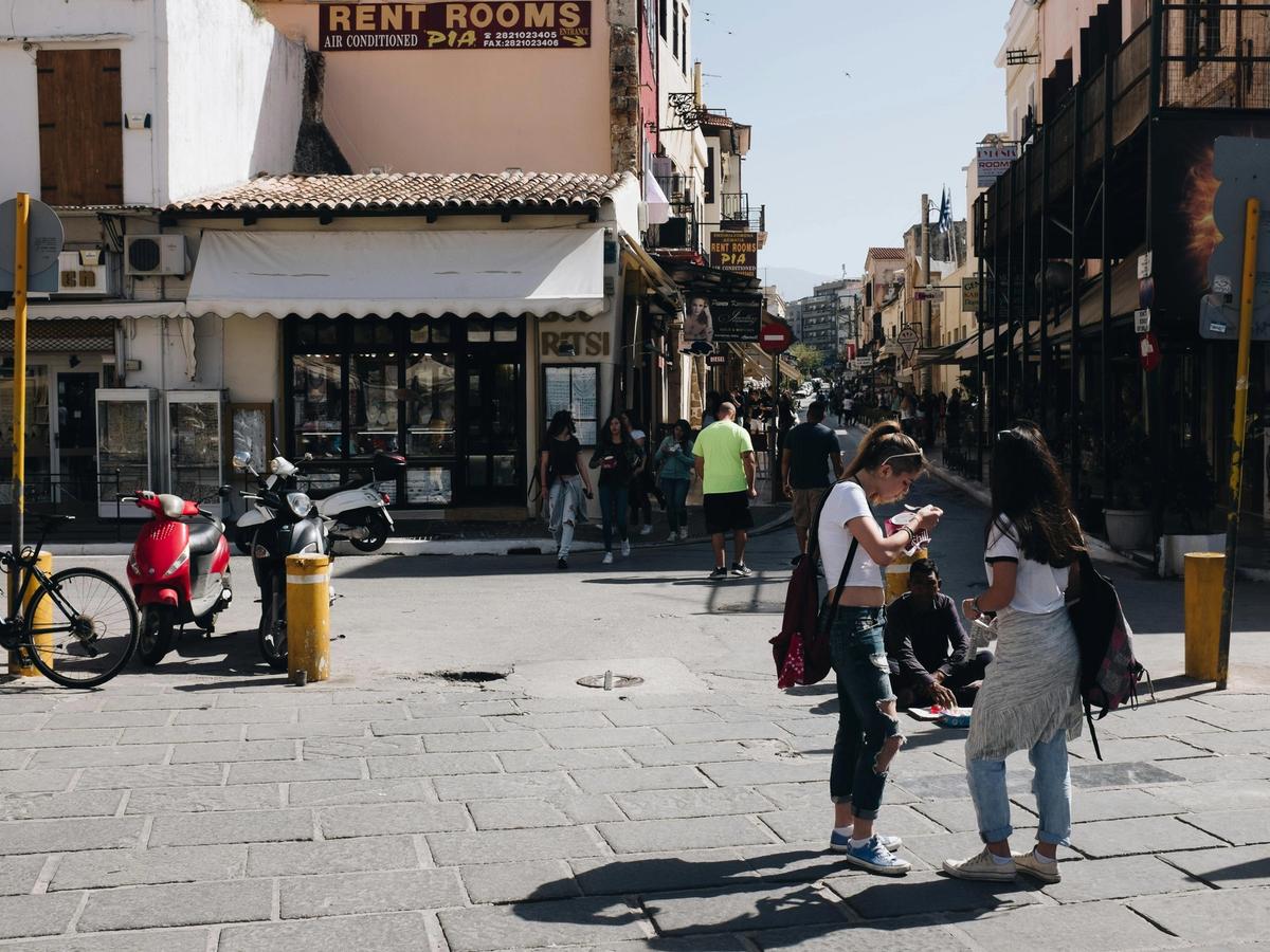 A lively city street filled with people walking, chatting, and exploring local shops. Motorbikes line the sidewalk, capturing the energy of everyday travel life.