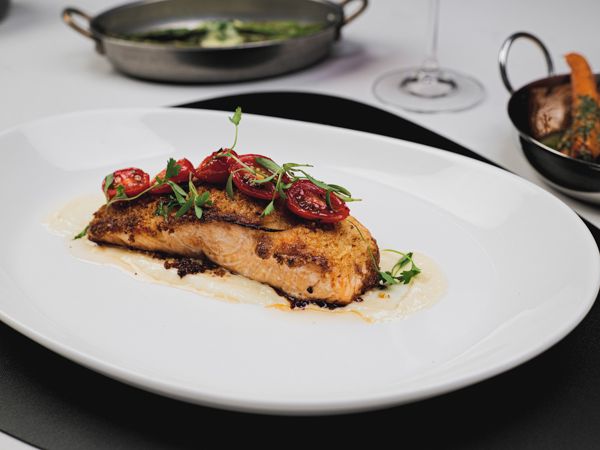Pan-seared salmon topped with roasted tomatoes and microgreens, served on a bed of creamy sauce. A modern fine-dining seafood dish that looks as good as it tastes.