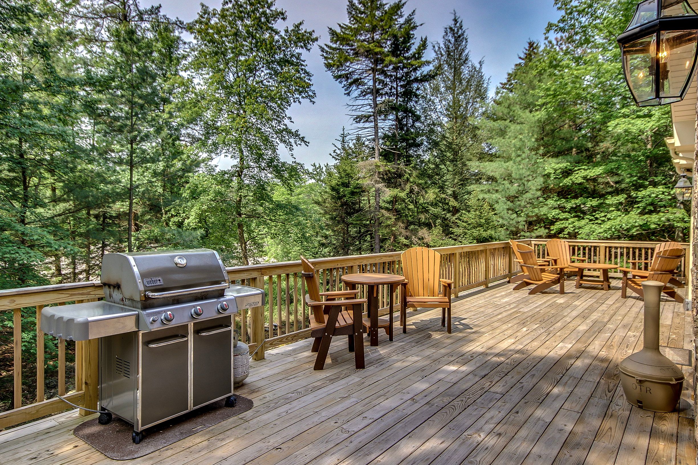 Spacious wooden deck with a stainless steel grill, Adirondack chairs, and forest views, perfect for outdoor dining and relaxation.