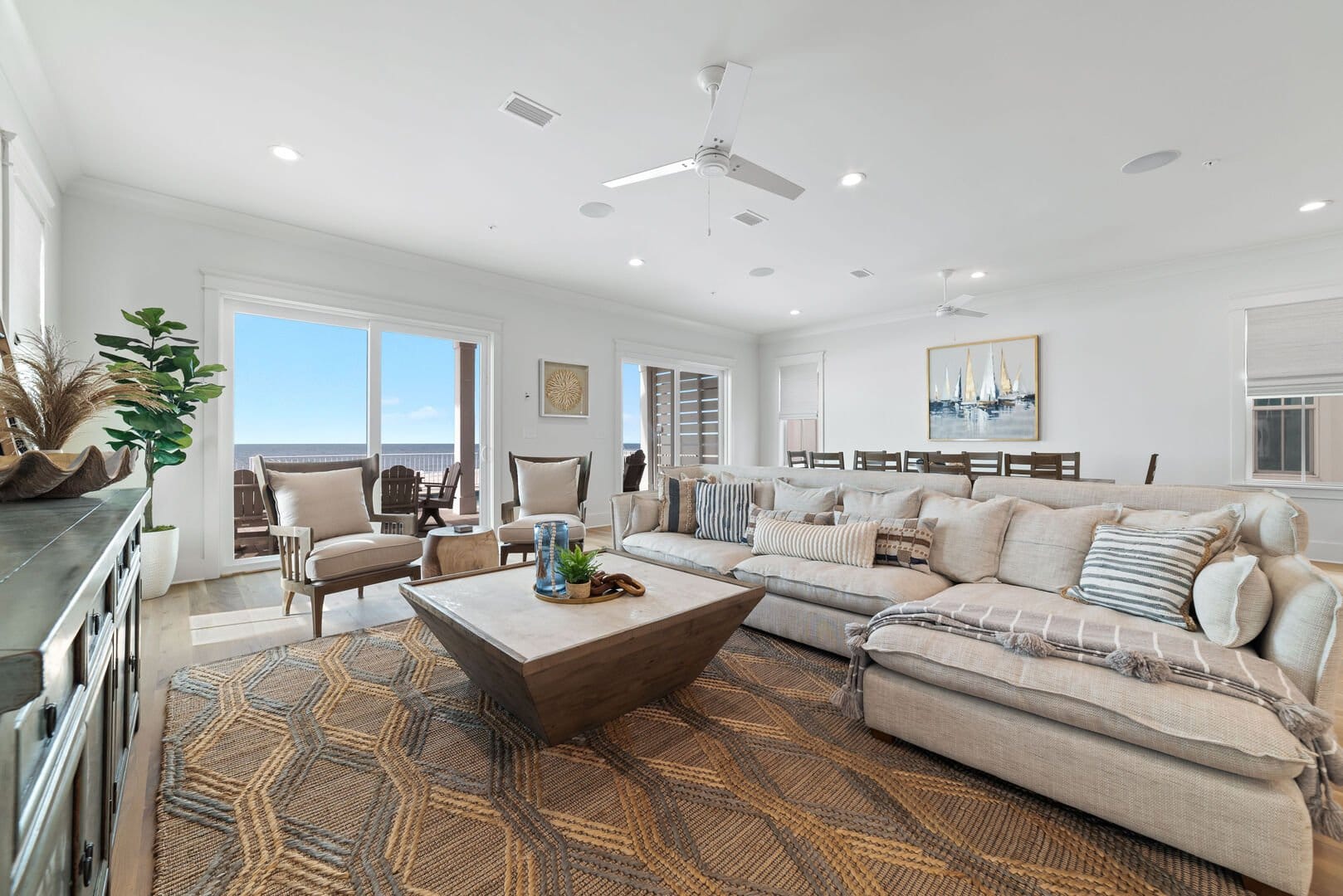 Coastal living room with a large sectional sofa, patterned rug, and wood coffee table facing sliding doors that open to ocean views.