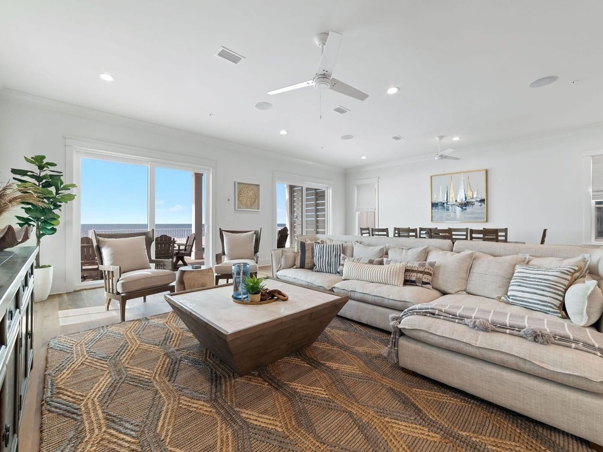Coastal living room with a large sectional sofa, patterned rug, and wood coffee table facing sliding doors that open to ocean views.