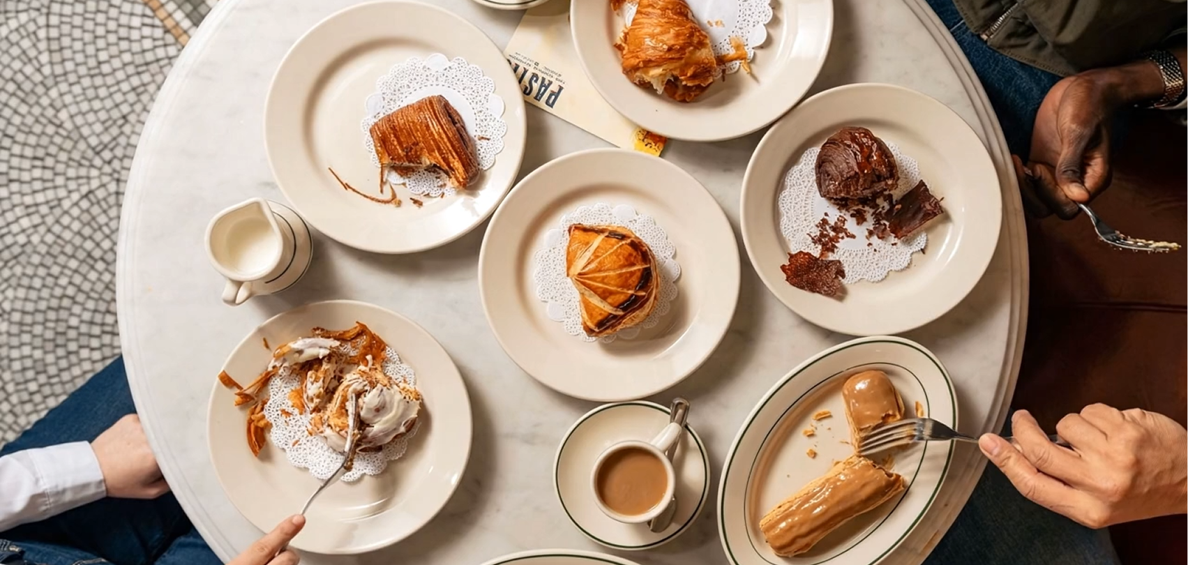 A beautiful spread of pastries and coffee is arranged on a marble table, showing flaky layers, rich fillings, and sweet toppings. The warm tones make the treats look fresh and comforting. It feels like a perfect morning stop for anyone who loves classic baked goods.