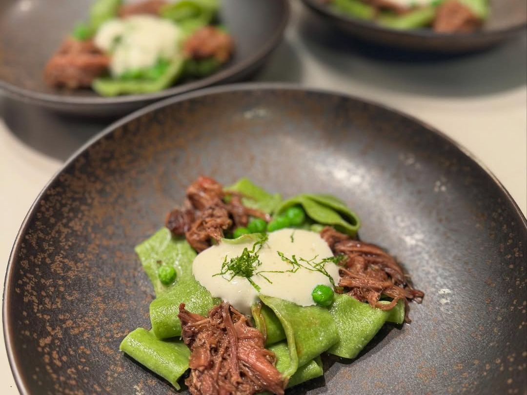 Gourmet pasta with slow-braised beef, fresh green peas, and creamy sauce, beautifully plated for an elevated dining experience.
