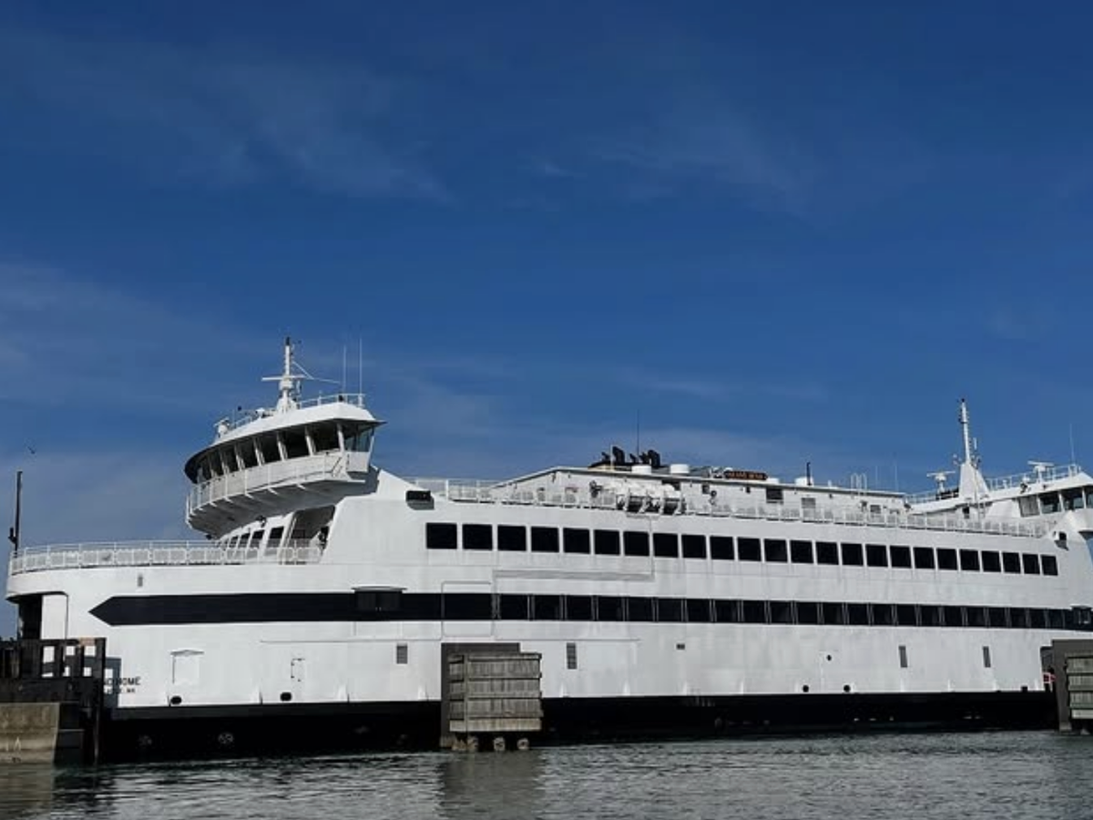 A large white passenger and vehicle ferry docked at a terminal on a clear, sunny day, with calm waters and a deep blue sky in the background