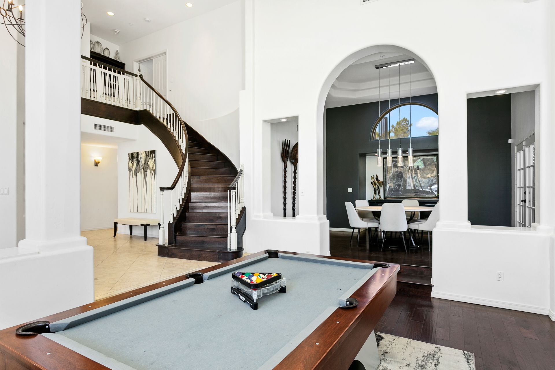 A grand, open-concept interior featuring a curved staircase, elegant dining nook, and a billiards table that adds a refined yet playful touch to the space.