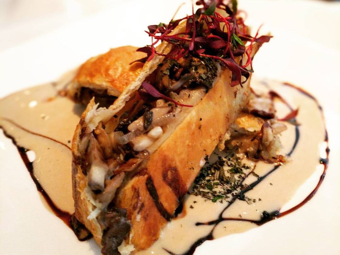 Golden pastry stuffed with mushrooms and vegetables, topped with herbs and plated with a creamy sauce. A gourmet dish that combines rich flavors with artistic plating.