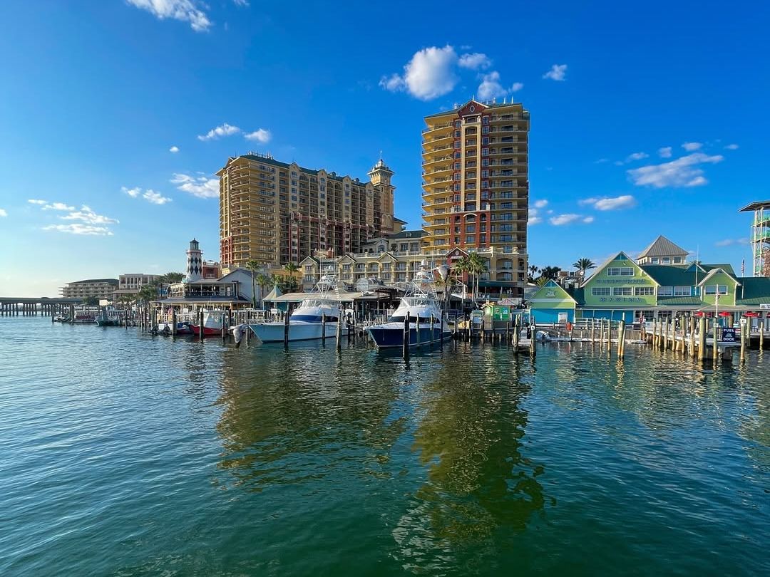 A waterfront view of Emerald Grande at HarborWalk Village with yachts docked by colorful shops and luxury condos rising above the marina. A hub for dining, nightlife, and boating in Destin.