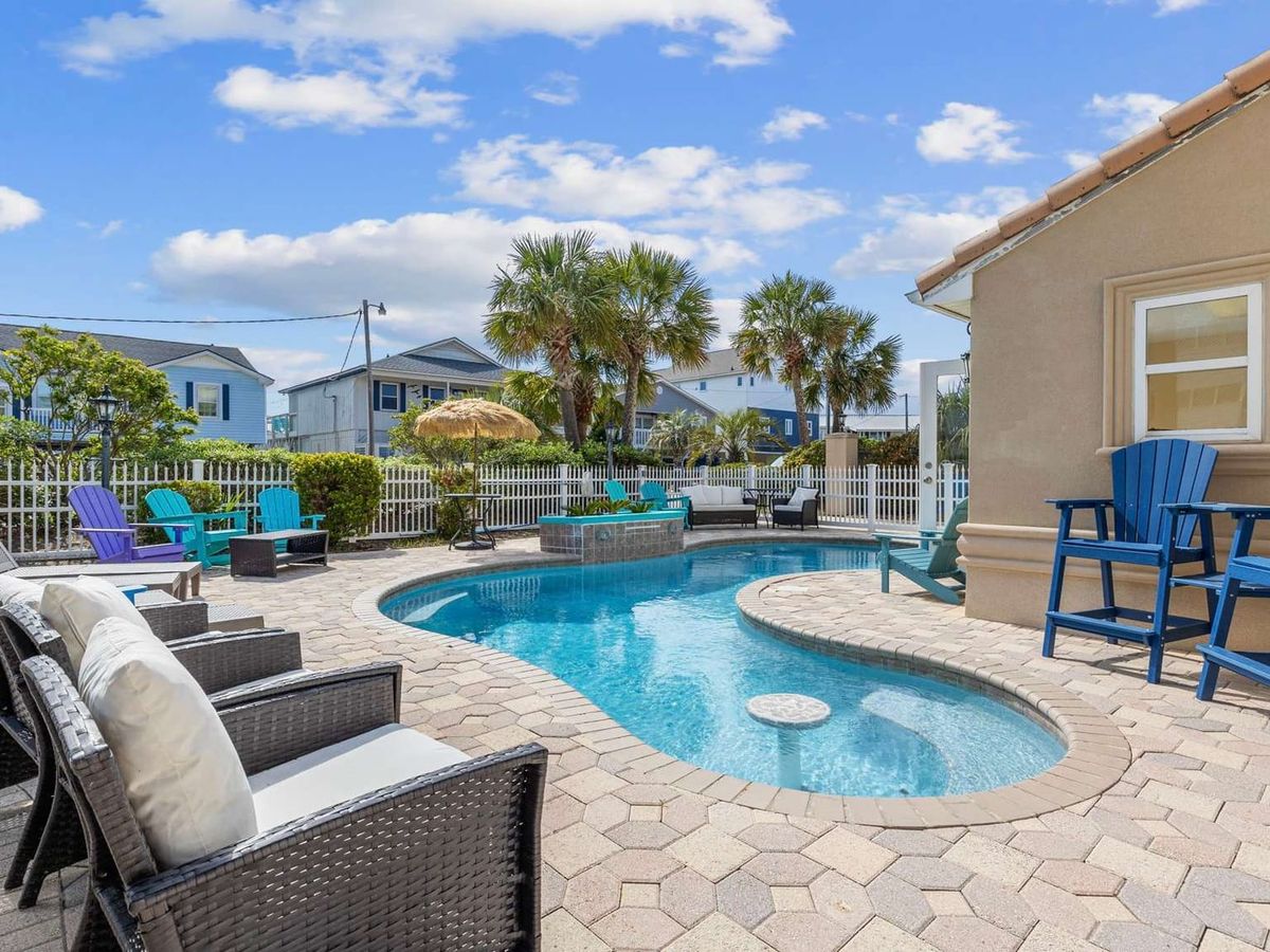 Palm trees frame this tropical backyard complete with a pool, hot tub, and bright red umbrellas. It’s a dreamy North Myrtle Beach escape where big families gather to relax, grill, and enjoy golden sunsets.