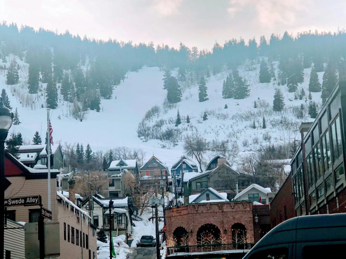 Snowy hillside dotted with pine trees rises behind charming mountain homes and storefronts on a wintry street in Park City, Utah, with the "Swede Alley" sign in view.