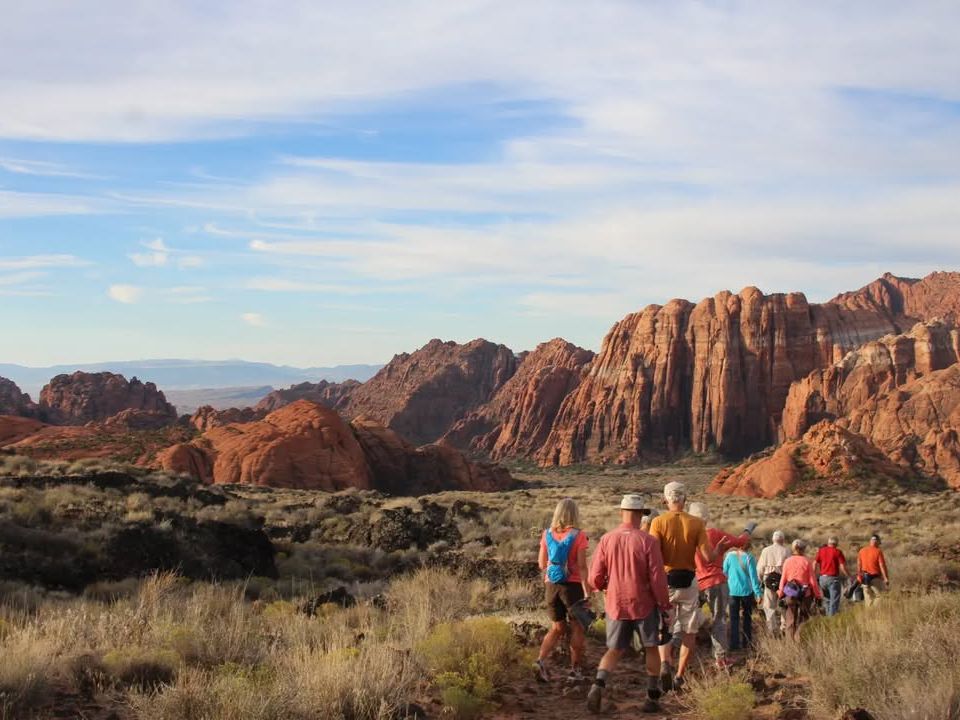 A group of visitors hikes across the petrified sand dunes of Snow Canyon State Park, showcasing unique rock formations shaped by nature.