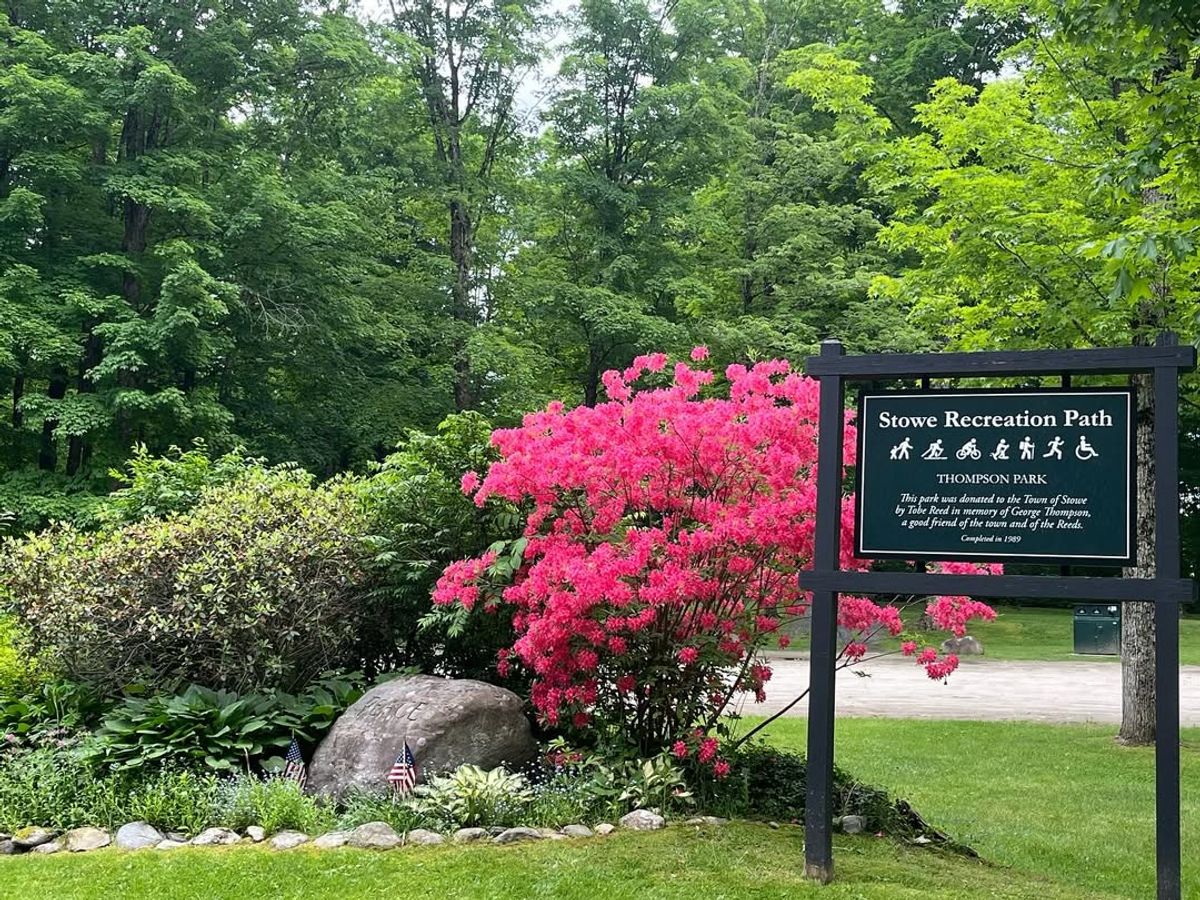 Colorful blooms and lush greenery welcome visitors at the entrance to Stowe Recreation Path. The sign for Thompson Park stands beside bright pink azaleas, marking the start of a scenic trail loved by walkers, bikers, and families year-round.