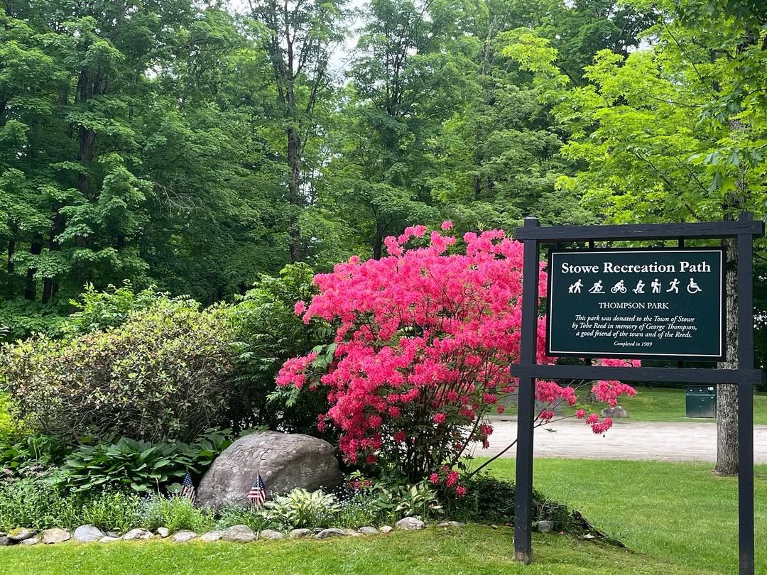 Colorful blooms and lush greenery welcome visitors at the entrance to Stowe Recreation Path. The sign for Thompson Park stands beside bright pink azaleas, marking the start of a scenic trail loved by walkers, bikers, and families year-round.