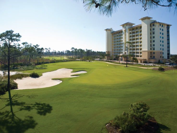 The lush fairways and sand traps of Lost Key Golf Club sit beside a tall resort building, offering golfers a championship course surrounded by natural beauty.