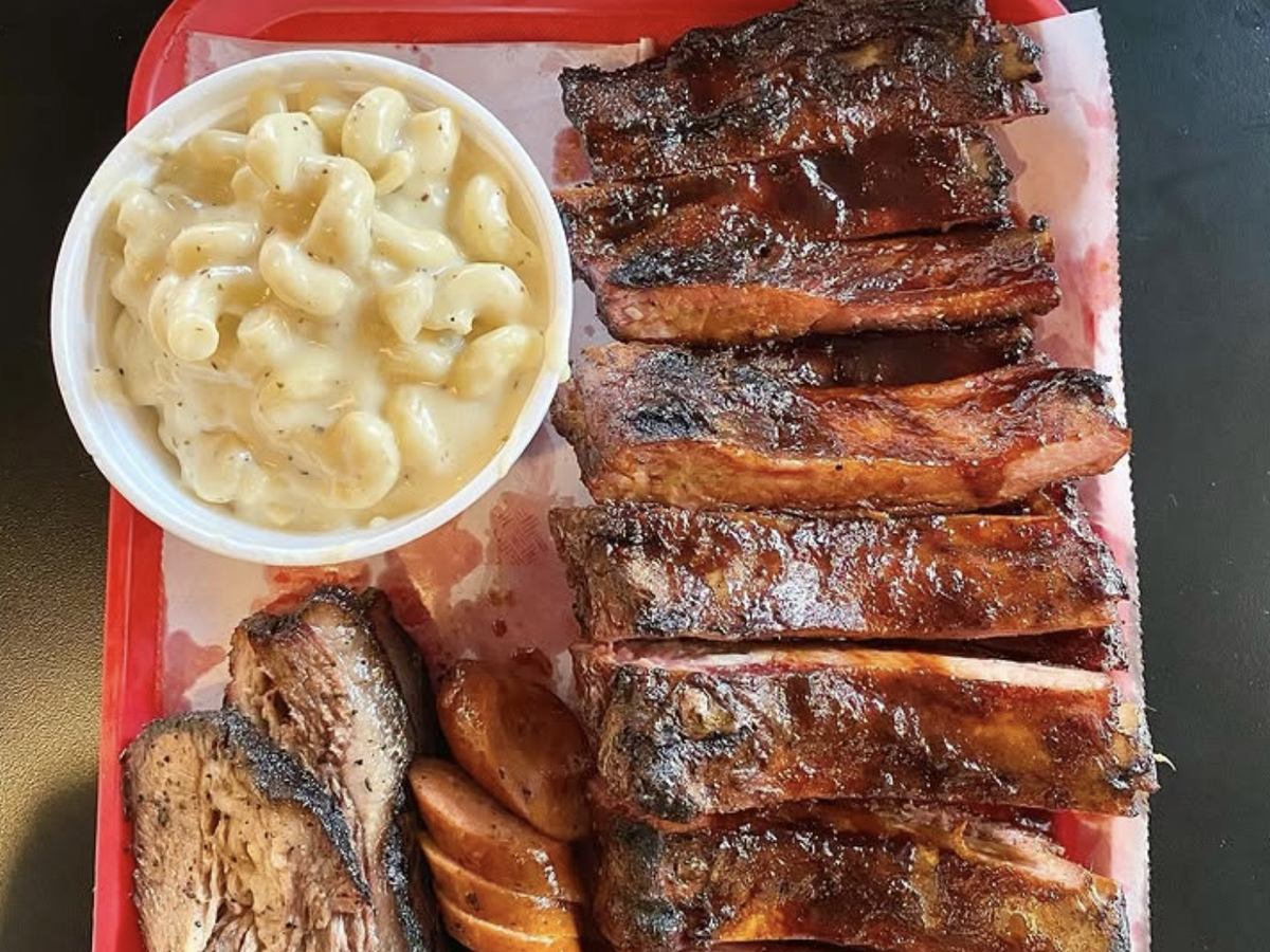 BBQ platter featuring glazed pork ribs, smoked brisket, sausage slices, and a side of creamy macaroni and cheese.