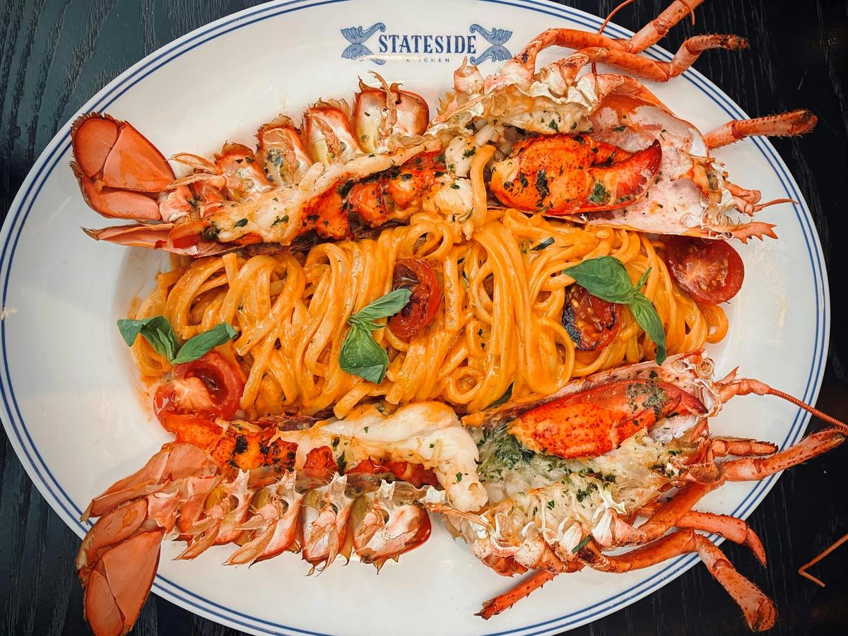 A luxurious seafood pasta dish featuring rich lobster halves atop creamy linguine with herbs and cherry tomatoes. Served on elegant white dinnerware, it’s a feast for both the eyes and the palate.