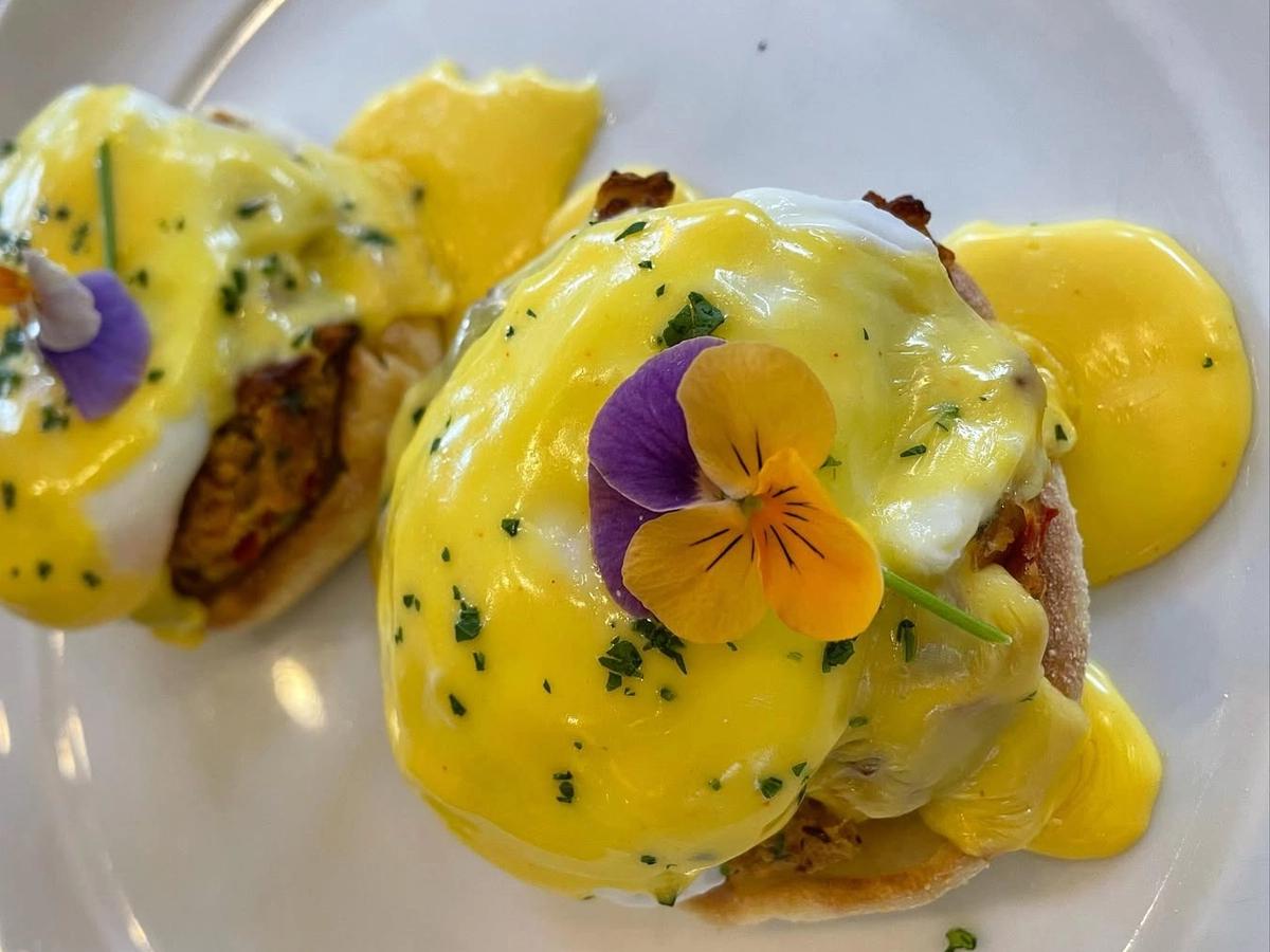 Close-up of gourmet eggs benedict topped with creamy hollandaise sauce and edible flowers, served on toasted English muffins for a vibrant and indulgent breakfast plate.