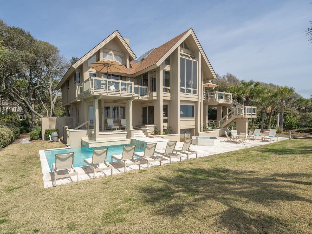 A luxury beachfront home featuring a modern design with multiple balconies and a pool overlooking the ocean. Comfortable lounge chairs and open spaces create the perfect setting for effortless relaxation and convenience.