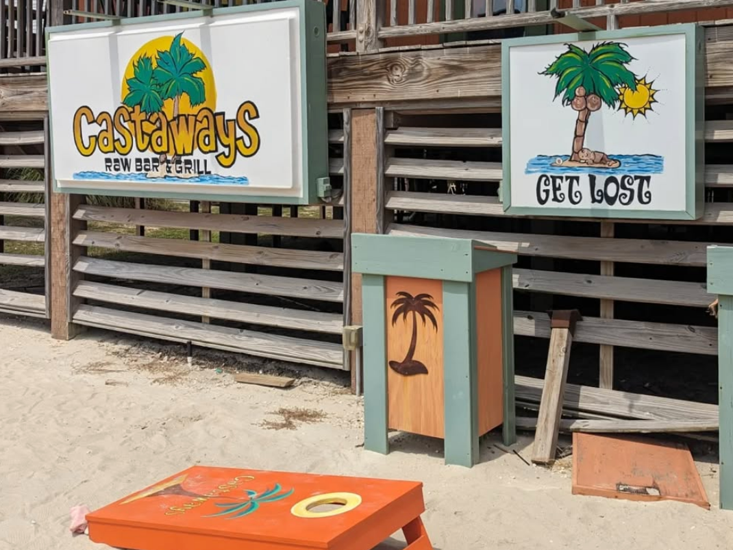 Orange cornhole board with palm tree on it and castaways sign in the background