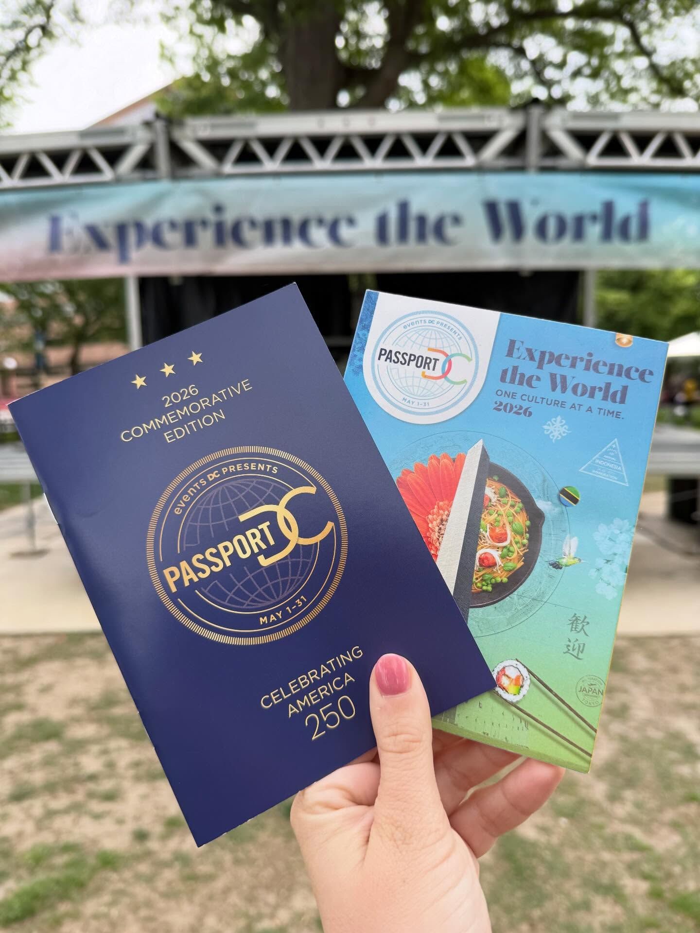 A hand holds up the 2026 Commemorative Edition Passport DC booklet and cultural guide in front of an "Experience the World" event banner, promoting the annual month-long embassy open house festival presented by Events DC in Washington.