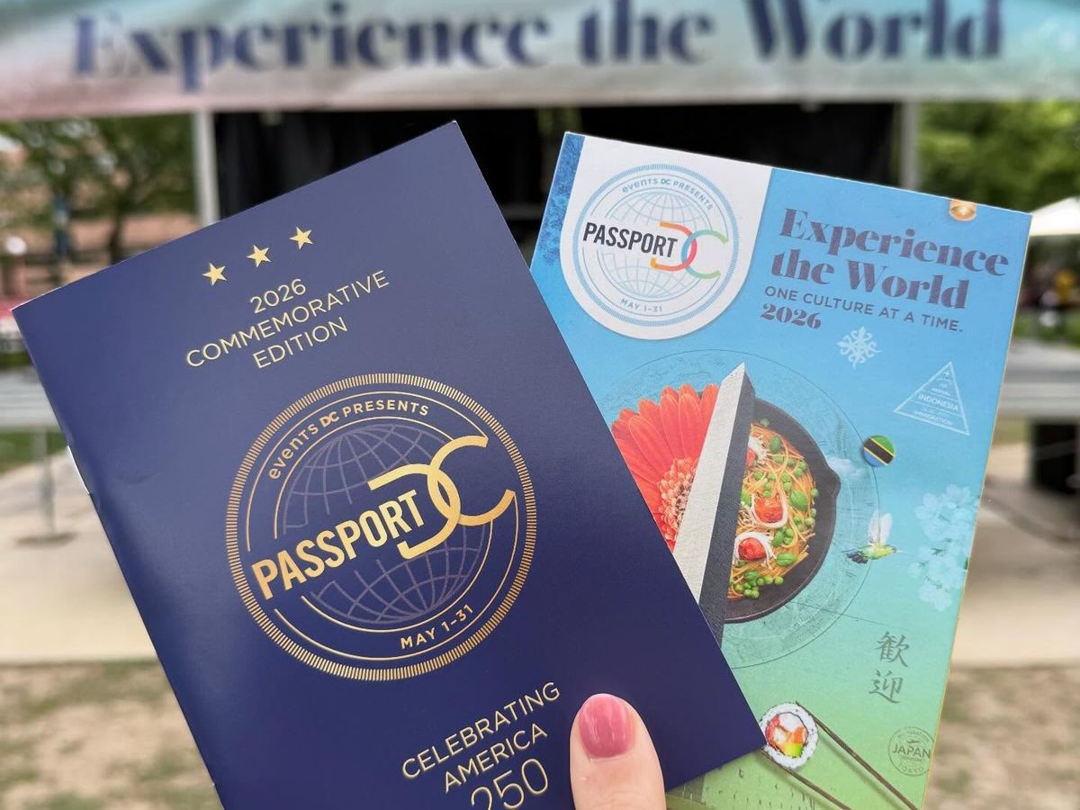 A hand holds up the 2026 Commemorative Edition Passport DC booklet and cultural guide in front of an "Experience the World" event banner, promoting the annual month-long embassy open house festival presented by Events DC in Washington.