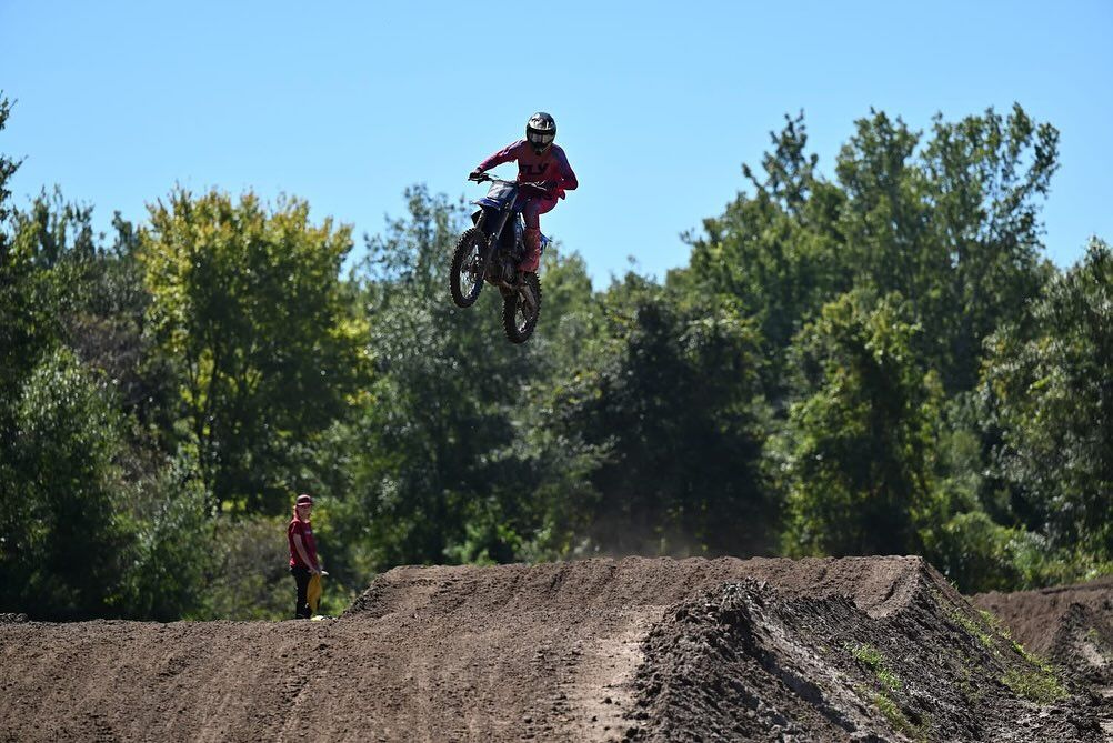 A motocross rider soars high above a dirt track while another looks on, surrounded by lush green trees. The energy and adventure make Ormond Beach a playground for thrill-seekers and families alike.