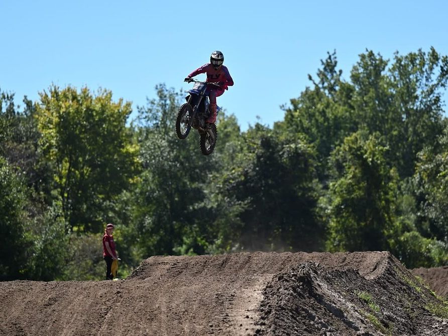 A motocross rider soars high above a dirt track while another looks on, surrounded by lush green trees. The energy and adventure make Ormond Beach a playground for thrill-seekers and families alike.