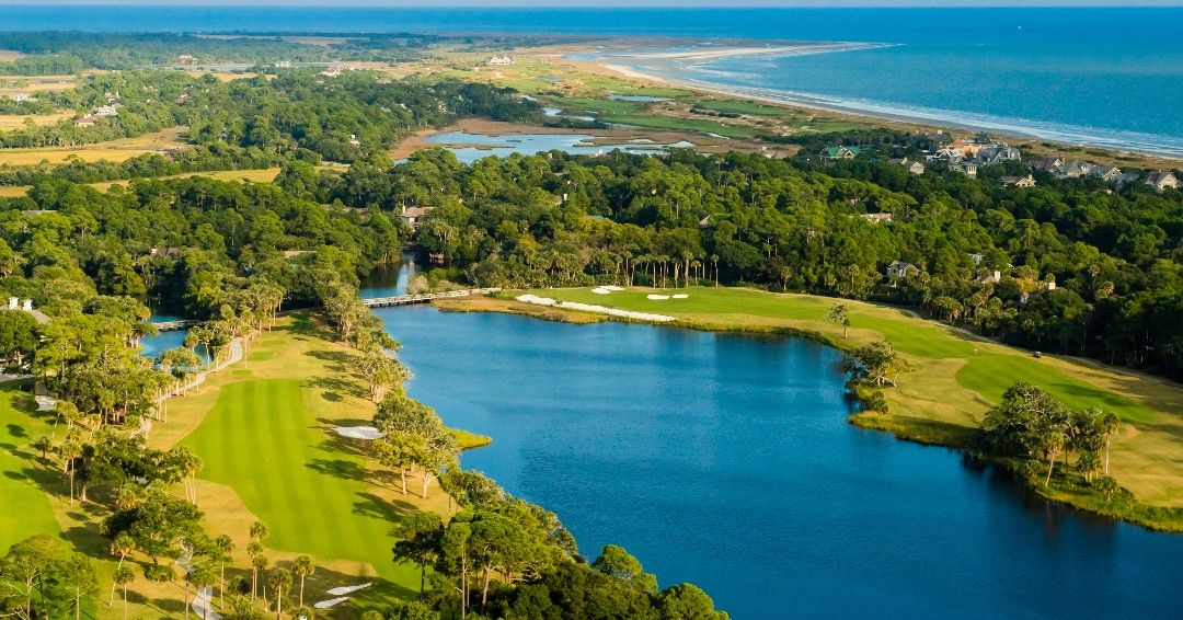 An aerial view of a stunning Kiawah Island golf course, with bright green fairways wrapped around calm blue water. The wide coastline stretches out in the distance, making the scene feel peaceful and open. It’s the kind of place where you can enjoy a slow, beautiful round of golf surrounded by nature.
