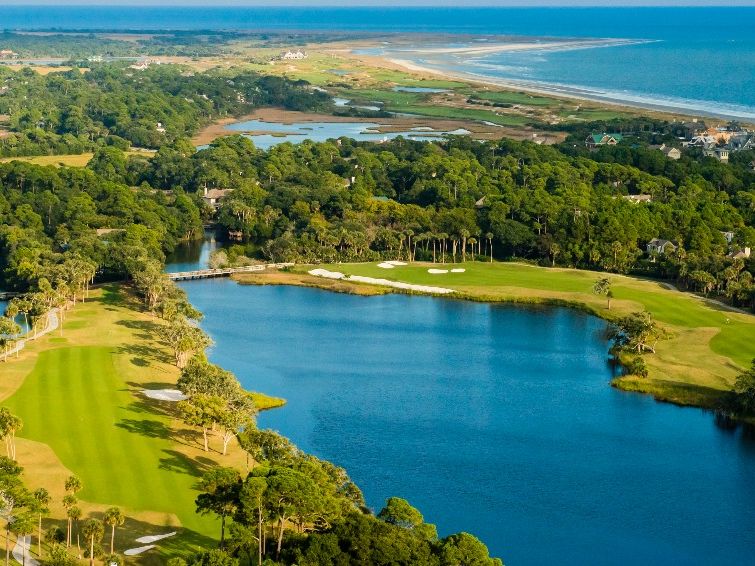An aerial view of a stunning Kiawah Island golf course, with bright green fairways wrapped around calm blue water. The wide coastline stretches out in the distance, making the scene feel peaceful and open. It’s the kind of place where you can enjoy a slow, beautiful round of golf surrounded by nature.