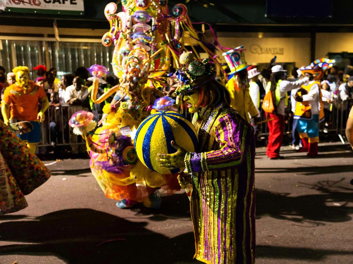 Man in street festival parade with his face painted, holding a yellow and blue ball
