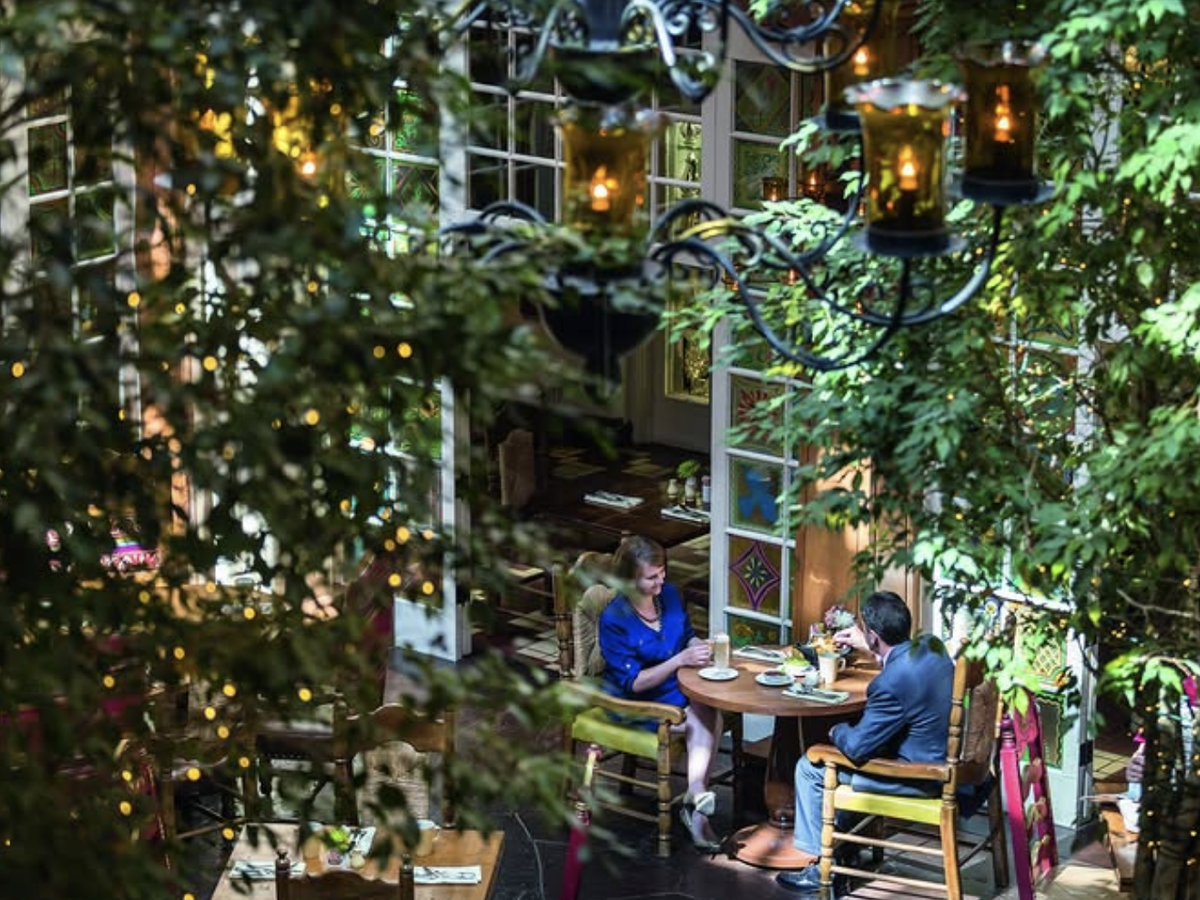 A couple dining at a cozy, greenery-filled restaurant with twinkling lights and a warm, intimate atmosphere.