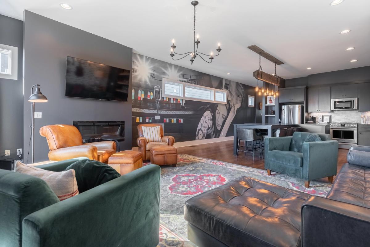 A spacious modern living area with leather and velvet seating, a bold wall mural, flat-screen TV, and an open-concept kitchen with stainless steel appliances.